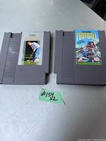 Photo of two vintage Nintendo NES game cartridges placed side by side on a metal surface. Left cartridge is Lee Trevino's Fighting Golf, right cartridge is NFL Football.