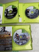 Three Xbox 360 game discs open in green cases: Call of Duty MW3 disc, Halo 4 disc 1 and 2, Battlefield 4 disc 1 and 2 with Premium insert visible.
