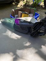 Photo of a Bissell hand vacuum cleaner with a purple accent and long black power cord, placed on a white surface outdoors.