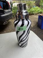 Photo of art glass cocktail shaker with black and white zebra style stripes and shiny chrome top in natural light