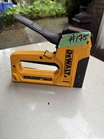 Side view of yellow and black DeWalt stapler with lever and branding visible, placed on white surface with outdoor background.