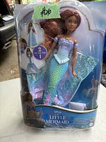 Image of the sealed boxed Disney The Little Mermaid Ariel 2-in-1 doll showing the doll with red hair and mermaid tail inside retail packaging.
