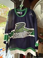 Photo of navy blue Florida Everblades hockey jersey hanging, showing front with team logo and sleeve patches.