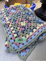 Folded hand knitted crocheted blanket showing multicolored granny square pattern in green, blue, pink, and cream yarns.