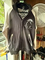 Full front view of the varsity jacket showing black body, off-white sleeves, ribbed black collar and cuffs, front pockets with white trim.