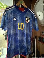 Front view of blue Japan national team soccer jersey with number 10 and Adidas logo, hung on hanger.
