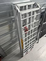 Folded cast aluminum motorcycle loading ramp standing upright showing grid design and folding hinge.