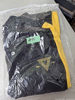 Folded black sweatpants with yellow stripes, visible triangle logo, sealed in a clear plastic bag with price tag '#95' attached.