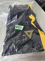 Black sweat pants with yellow stripe and logo folded inside clear plastic bag labeled #87m