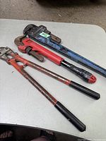 Wide photo showing three vintage hand tools: one large blue pipe wrench, one smaller red Milwaukee pipe wrench, and a vintage bolt cutter with long red handles.