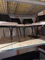 Four black wooden back chairs with light beige seats and black metal legs placed on shelving.