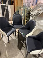 Four black and white chairs arranged in a semi-circle showing front and side views, located in a storage area with various other items in the background.
