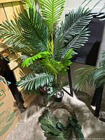 Full view of artificial green leaf plant in vase, wreath visible on floor.