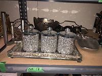 Three hammered metal canisters with lids on a rectangular mirror tray, along with metal decorative bowls and stand.