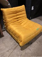 Side and front angle view of a yellow fabric lounge chair showing its tufted design and low-profile shape.