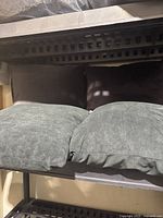 Four square cushions arranged in two rows on a metal shelf, two black cushions and two grey cushions in front.