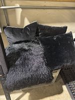 Four black cushions and pillows arranged on a surface, showing different fabric textures: velvety smooth and faux fur, used for decoration or staging.
