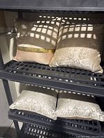 Two cushions with metallic gold bands and wavy patterns on top shelf, two beige marbled cushions on bottom shelf