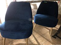 Two matching blue fabric side chairs with wooden legs positioned on wood flooring, showing general wear.