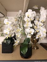 Photo of three faux white orchid flower arrangements placed side by side on a flat surface showing detail and size.