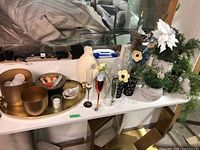 Full display of various faux plants, vases, glasses, large gold-tone metal tray with decorative bowls and light bulbs on table