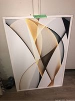Framed abstract wall art with white frame leaning on floor against wall.