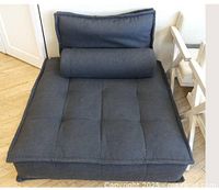 Front view of large anthracite modular armless chair with back and bolster cushions on a parquet wood floor.