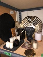 Photo showing assembled lot items including large metal filigree bowl, black trays, pillar candles, bust candleholder, reed diffuser and brass coasters.