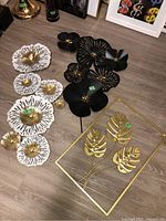 Overview photo showing all three metal wall art pieces arranged on the floor: white and gold floral set, black floral set, and gold leaves frame.