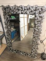 Front view of the rectangular wall mirror showing the decorative silver textured leaf-like frame and reflective mirror surface.