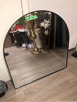 Full view of the arched wall mirror with a black metal frame placed on the floor showing the overall shape and size.