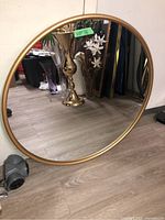 Front view of the round mirror showing full reflective surface and gold frame leaning against a wall on a wooden floor.