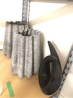 Three gray ceramic vases with textured wavy ribbed design and black metal curvy abstract sculpture on wooden surface by shelving unit.