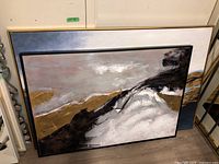 Two framed canvas paintings leaning against a wall with abstract landscape art, one with a golden frame and the other with a black frame.