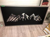 Framed abstract wall art with a black background and reflective mirror pieces forming jagged mountain shapes.