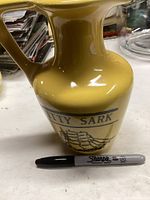 Yellow ceramic Cutty Sark pitcher with ship illustration and Sharpie marker for scale
