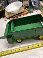 Photo showing the side view of the green John Deere bale wagon toy with yellow wheels, including a measuring tape below showing about 11 inches length.