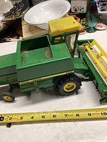 Side and top views of green and yellow Ertl John Deere 6600 combine toy showing dirt in hopper and attached yellow header.