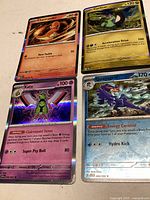 Photo showing all four Pokémon cards Charmander, Cyclizar, Xatu and Quaquaval with holographic shine and visible attack details.