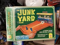 Front of the box showing game title The Junk Yard and illustration of pinball target gameplay with flippers and ball launcher.