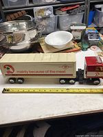 Side view of large vintage transport truck toy with red cab and beige trailer showing slogan and logo.