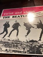 Front cover of the Beatles 'Twist and Shout' album showing the four band members mid-jump over a brick wall, album title and band name in bold lettering on a colorful background.