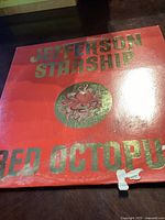 Front of the Jefferson Starship 'Red Octopus' vinyl record sleeve, red background with metallic green text and octopus logo, showing minor wear and a small paper tear at bottom right.