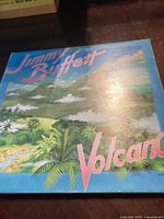 Front cover of Jimmy Buffett's 'Volcano' album showing tropical landscape and volcano illustration.