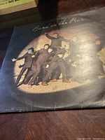 Front cover of Wings "Band on the Run" vinyl record album showing band members posing in dark clothing under spotlight.