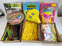 Photo showing 3 vintage child Halloween masks in original boxes: E.T., Big Bird, Cinderella. Masks are displayed with their fabric costumes removed from the boxes.