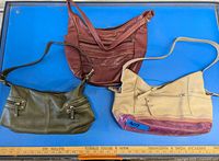 Three vintage leather purses displayed on a blue surface: red Tignanello, olive green The Sak, and cream with burgundy bottom trim purse.