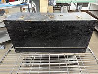 Closed view of the wooden antique carpenter's toolbox showing black paint with wear and scuff marks.