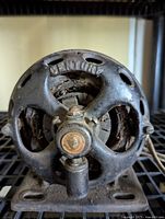 Front view of antique Invincible split phase motor showing ribbed metal housing with ventilation holes and central bolt.