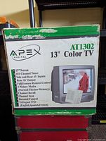 Box of Apex AT1302 13-inch color TV showing front with product details and features.